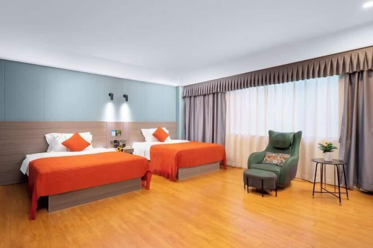 Una habitación de hotel con dos camas, un sillón verde, una mesita y una ventana con cortinas.