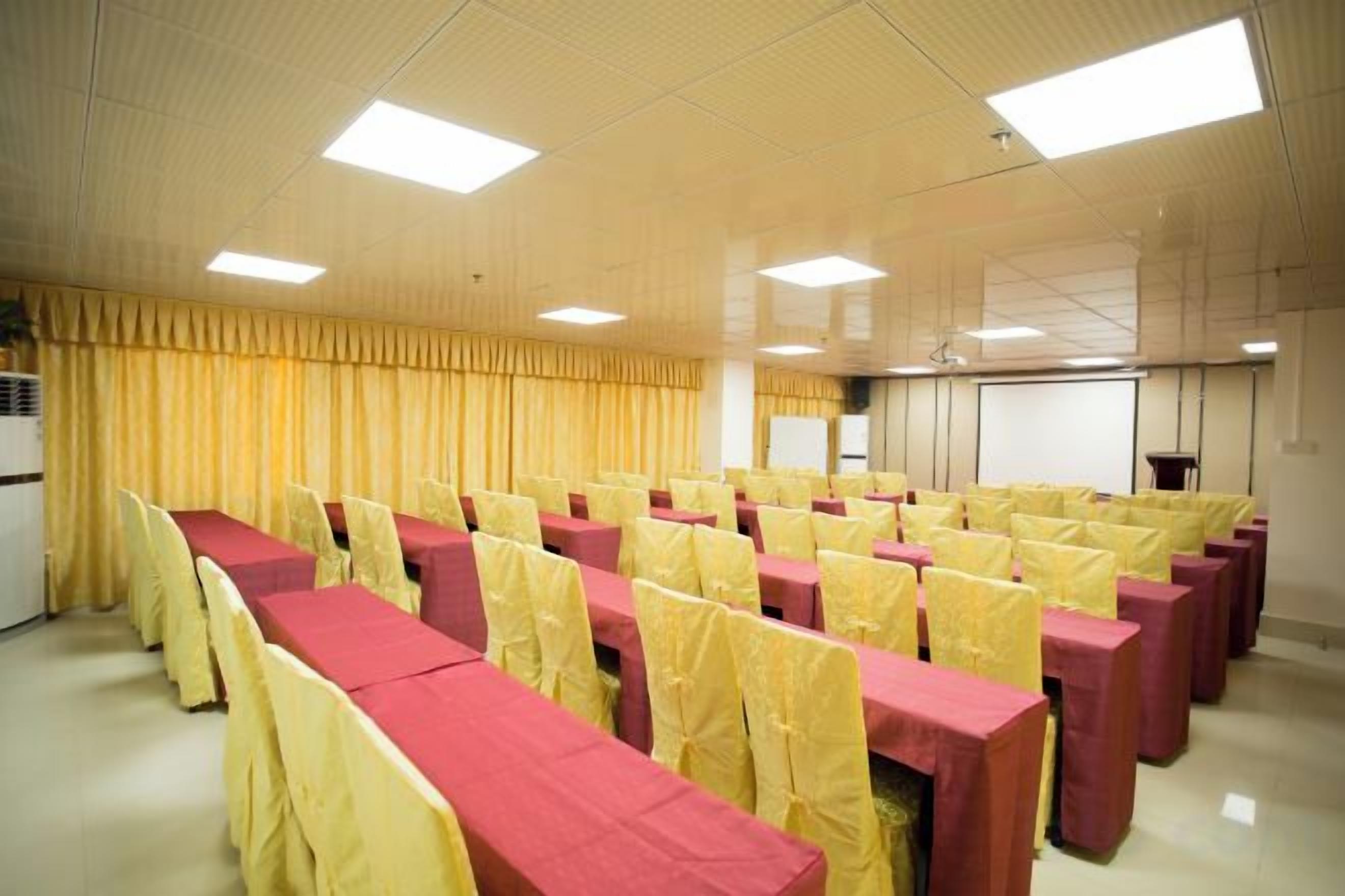 A conference room with rows of tables and chairs, a projector screen, and a whiteboard.