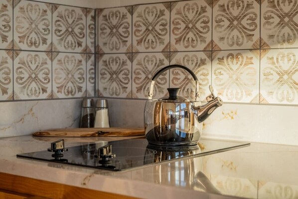 A kitchen with a glass-top stove, a kettle, and a wooden cutting board.