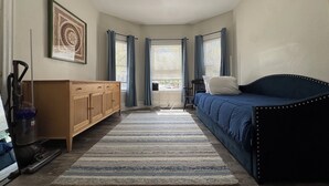 A bedroom with a bed, a dresser, a vacuum cleaner, and a window with curtains. - 2-bedroom apartment in fabulous Somerville with AC, WiFi and off street parking (Somerville)