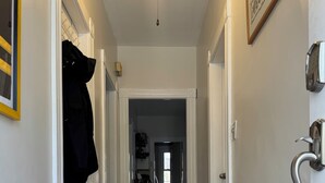 A hallway with a wooden floor, white walls, and a ceiling light. There is a door on the right with a silver handle and a framed picture above it. - 2-bedroom apartment in fabulous Somerville with AC, WiFi and off street parking (Somerville)