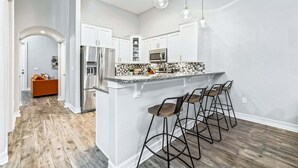 Une cuisine moderne dotée d’un îlot central, de tabourets de bar, d’appareils électroménagers en acier inoxydable et d’un plancher en bois.