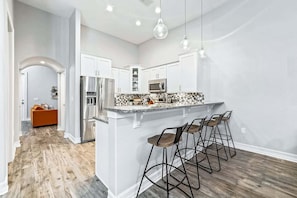 A modern kitchen with a central island, bar stools, stainless steel appliances, and a wooden floor.
