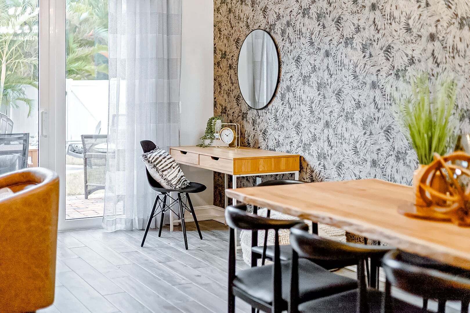 A dining area with a wooden table, black chairs, a striped chair, a clock, and a mirror on the wall.