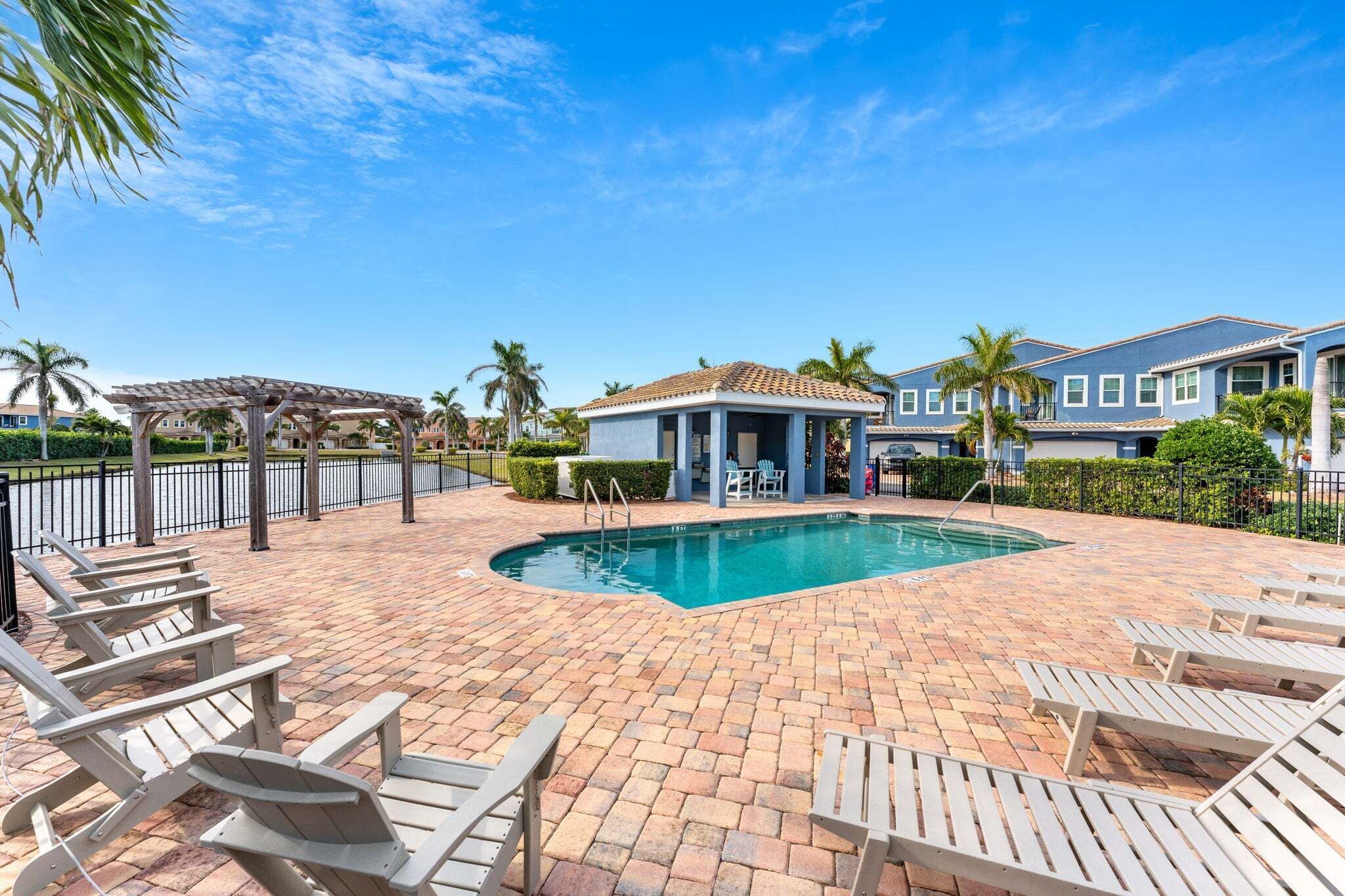 A pool area with lounge chairs, a covered seating area, and a building with a tiled roof.