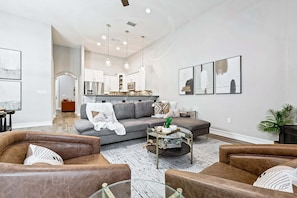 A modern living room with a sofa, two armchairs, a coffee table, and a kitchen in the background.