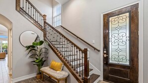 Un escalier avec des balustrades en bois, un banc avec un coussin, une plante en pot et une porte ornée d’un panneau de verre décoratif.