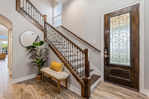 A staircase with wooden balusters, a bench with a cushion, a potted plant, and a door with a decorative glass panel.