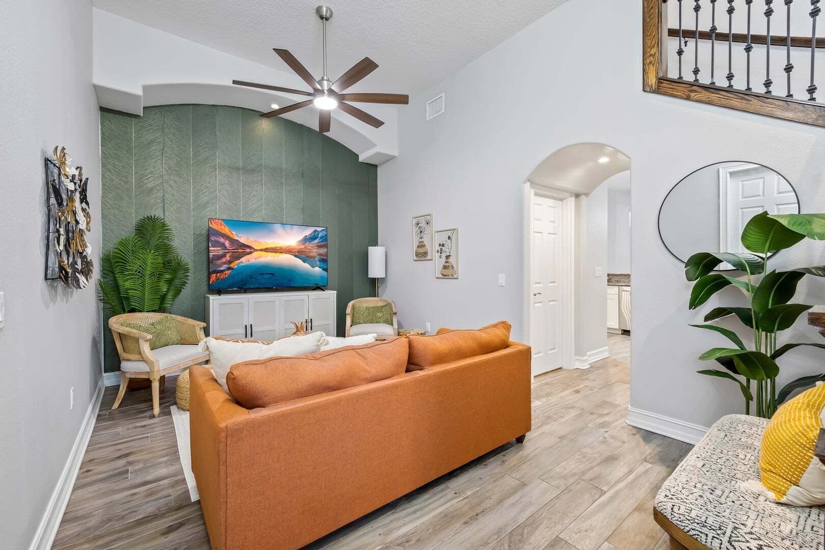 Un salon comprenant un canapé, un téléviseur, un ventilateur de plafond et des plantes décoratives.