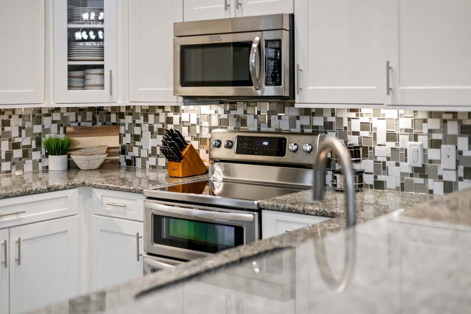 A modern kitchen with white cabinets, a stainless steel microwave, an oven, and a tiled backsplash.