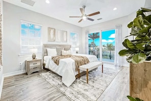 A bedroom with a bed, bedside tables, a ceiling fan, a large window with a view, and a balcony.