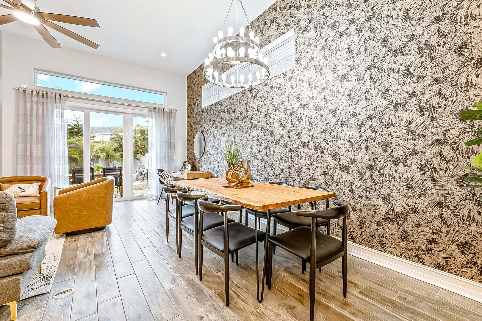 A dining area with a wooden table, black chairs, a chandelier, and a patterned wall.