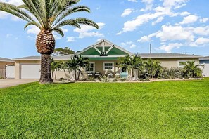 A house with a green roof, a garage, and a well-maintained lawn with a palm tree. - 445 Watts Way (Cocoa Beach)