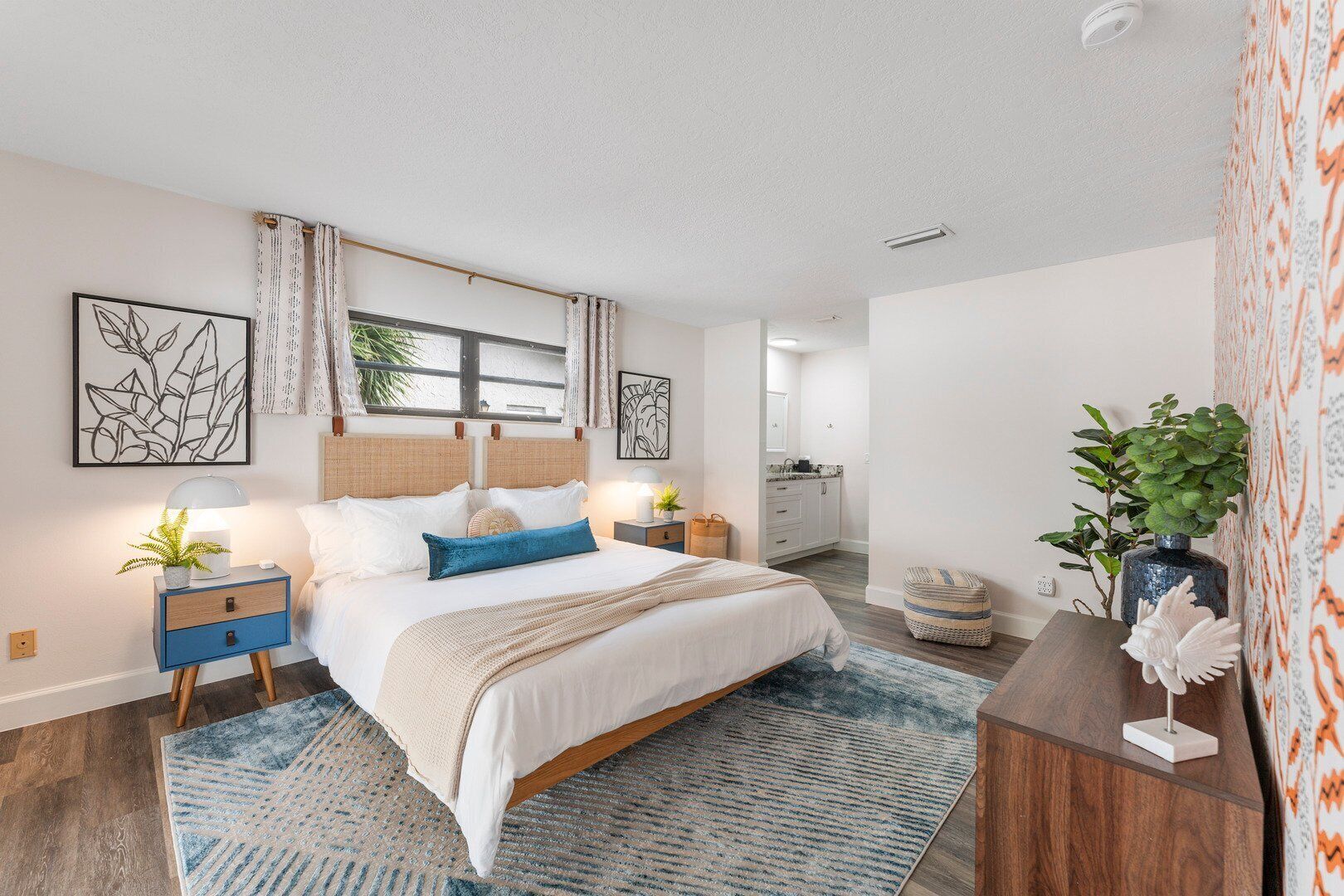 Een moderne slaapkamer met een groot bed, nachtkastjes, een dressoir en een raam met gordijnen.