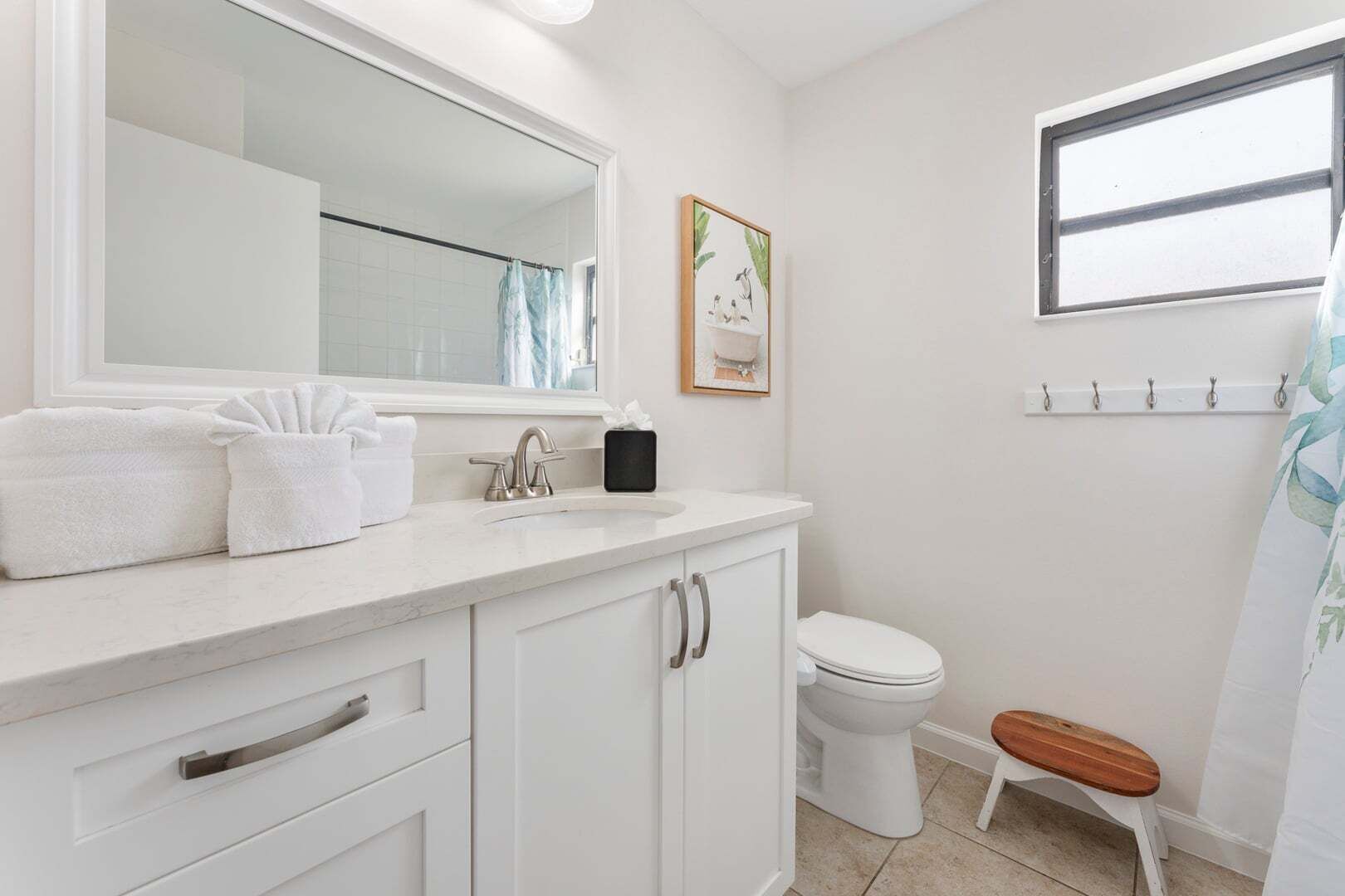 A bathroom with a white sink, mirror, and toilet. There is a small wooden stool and a towel rack.