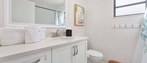 A bathroom with a white sink, mirror, and toilet. There is a small wooden stool and a towel rack.