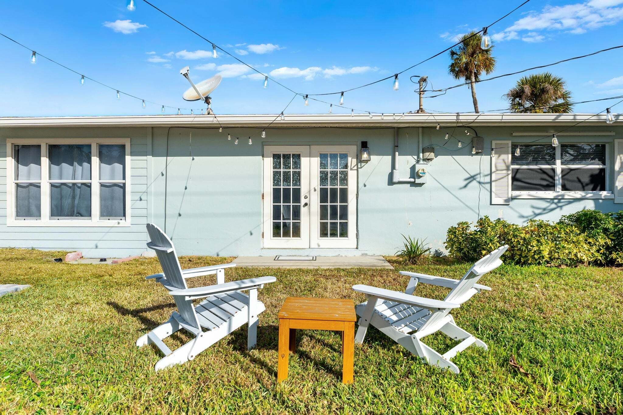 A house with a front porch, two white Adirondack chairs, a small wooden table, and a satellite dish.