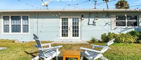 A house with a front porch, two white Adirondack chairs, a small wooden table, and a satellite dish.