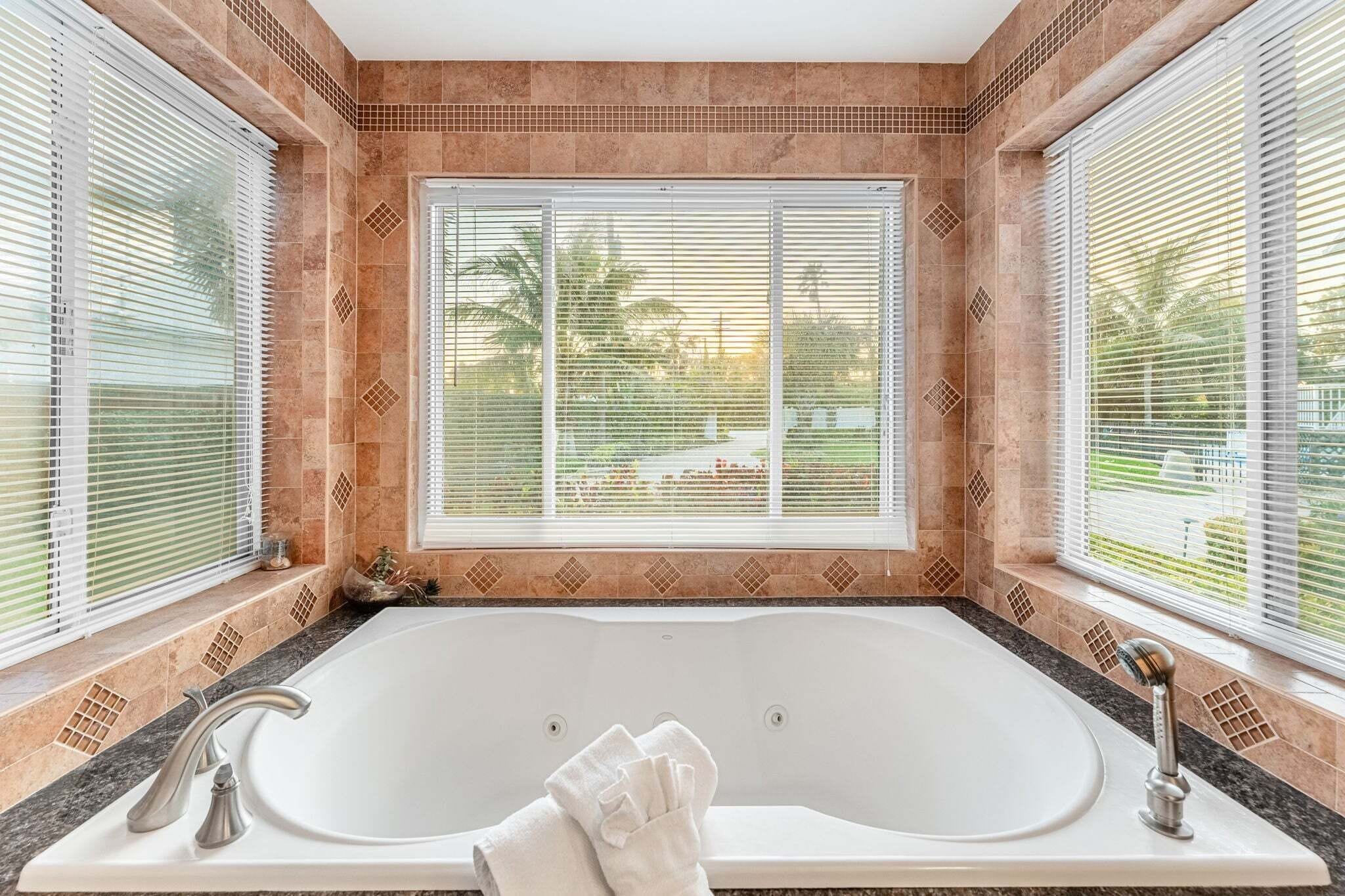 A bathroom with a bathtub, two faucets, and a window with blinds.