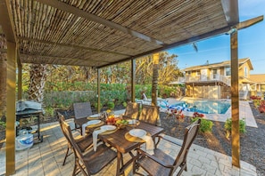 Un patio coperto con piscina, tavolo da pranzo, sedie e barbecue.