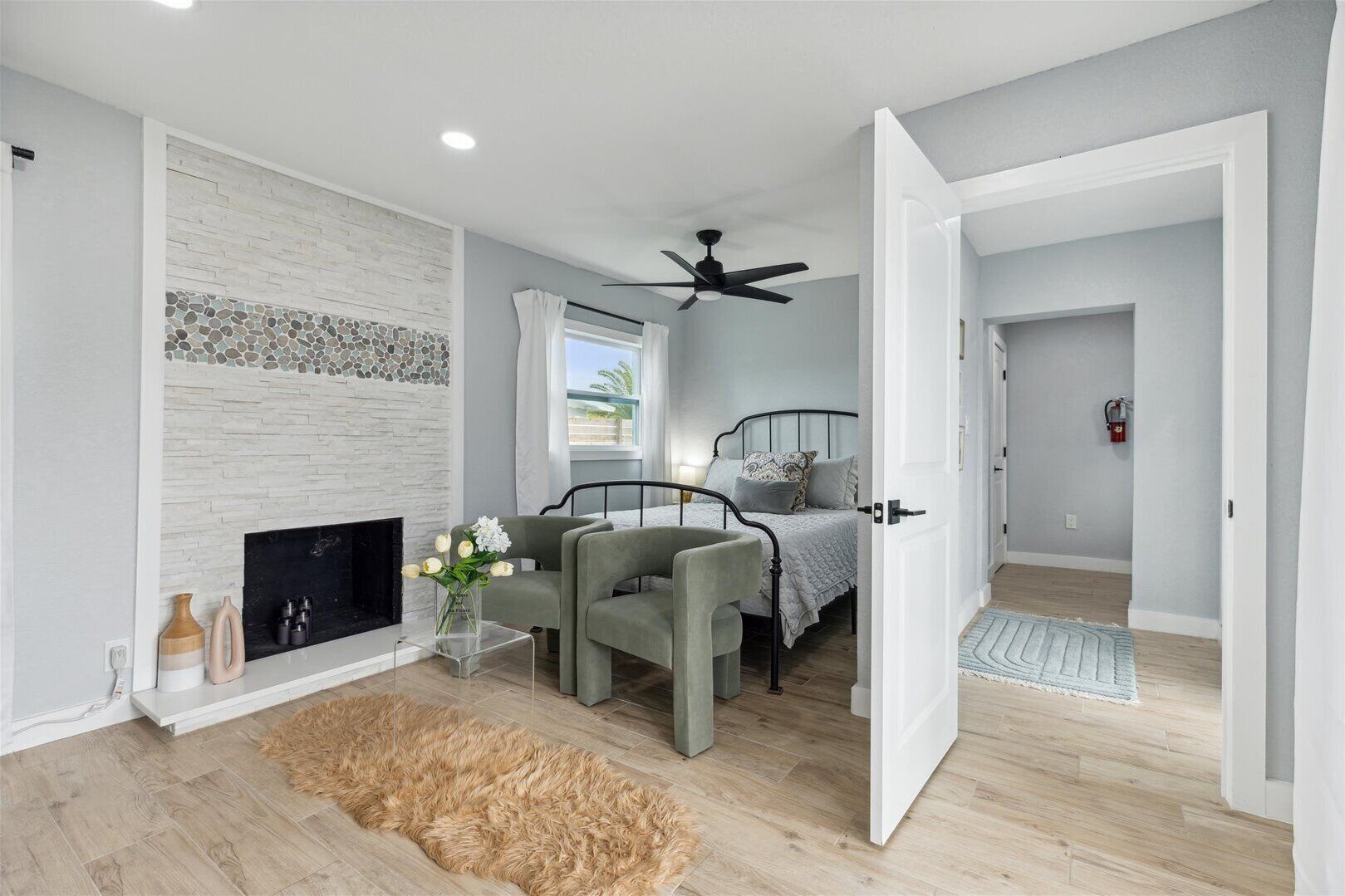 Quarto moderno com lareira, cama com cabeceira, ventilador de teto e vista para o exterior.