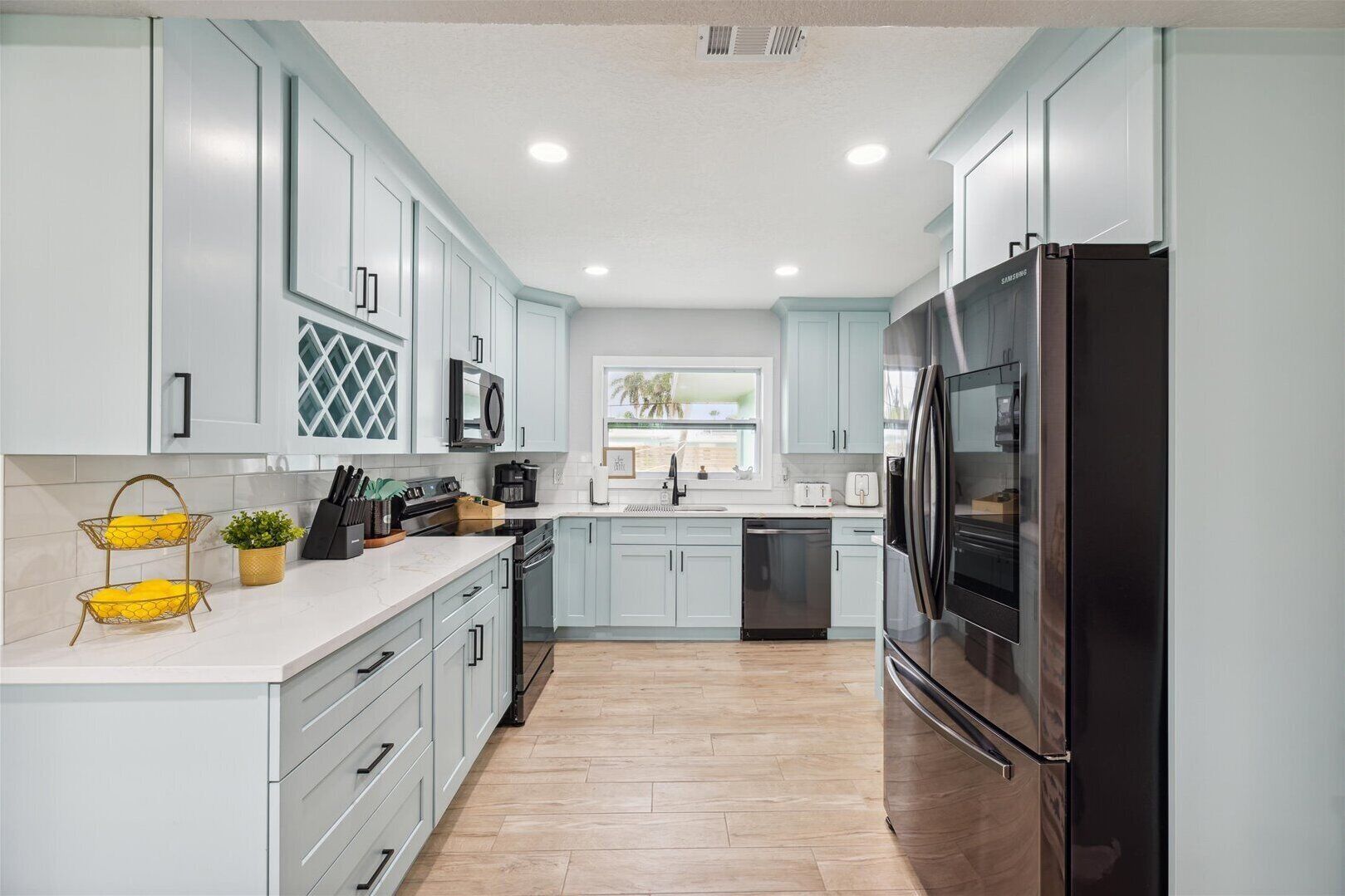 A modern kitchen with light blue cabinets, stainless steel appliances, and a wooden floor.