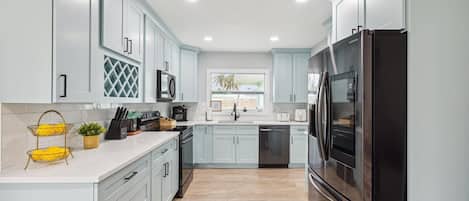 A modern kitchen with light blue cabinets, stainless steel appliances, and a wooden floor.