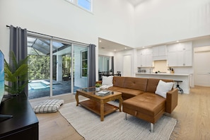 A modern living room with a glass coffee table, a brown leather sofa, and a view of a swimming pool through large glass doors. - 132 Ocean Estates Dr (Fort Pierce)