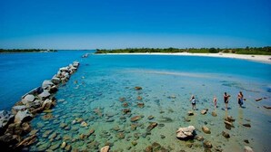 Ein klares, türkisfarbenes Meer mit einem steinernen Wellenbrecher und einem Sandstrand.