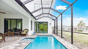 Ein überdachter Pool mit Glasveranda, Korbmöbeln und Blick ins Freie.