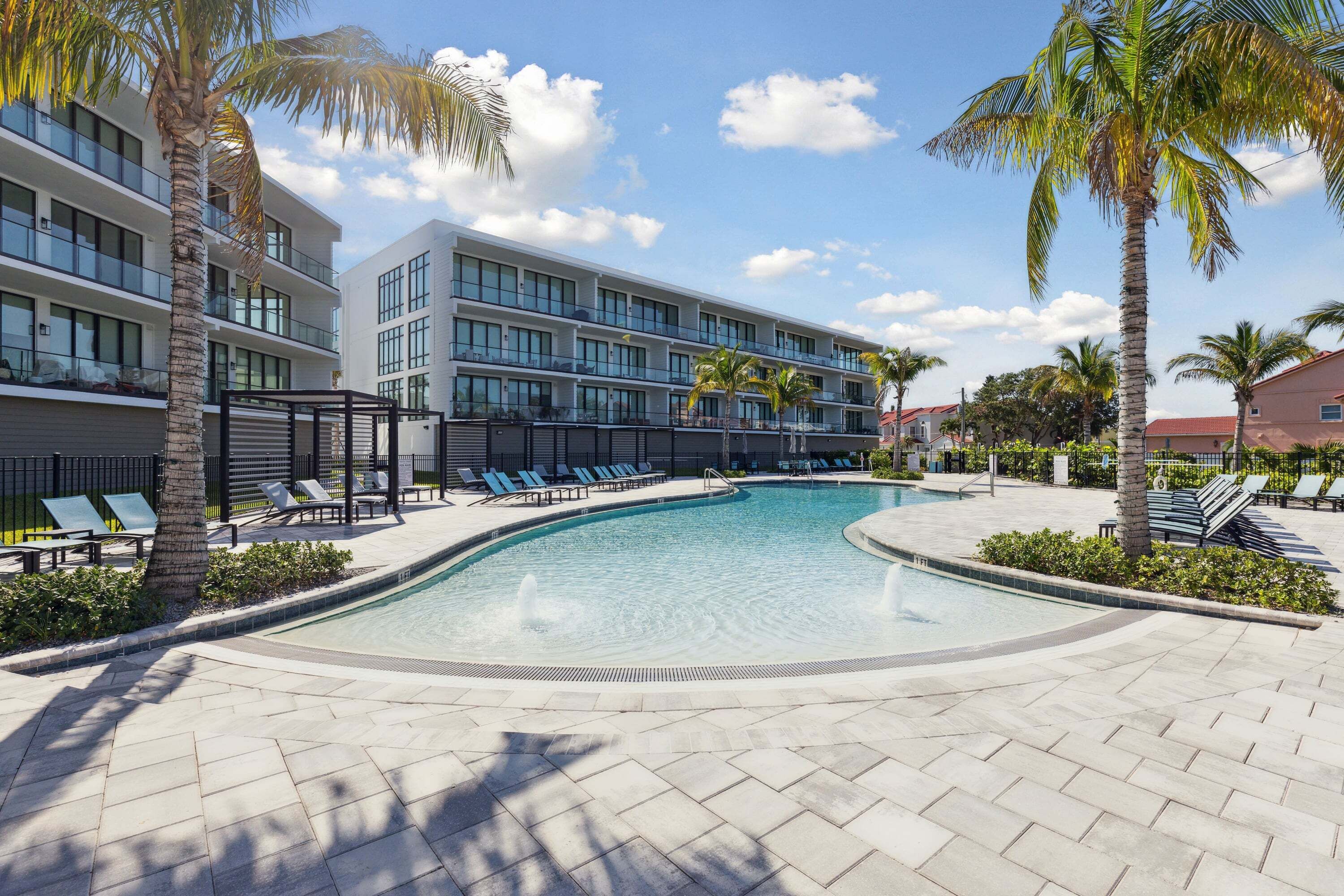 A swimming pool with lounge chairs, palm trees, and a modern building with balconies.