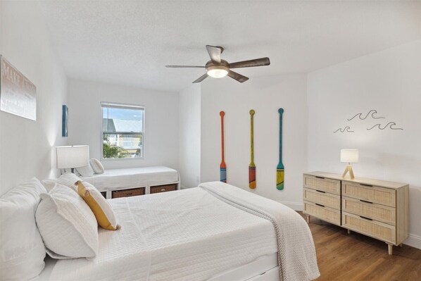 A bedroom with a bed, bedside tables, a dresser, a ceiling fan, and a window with a view.