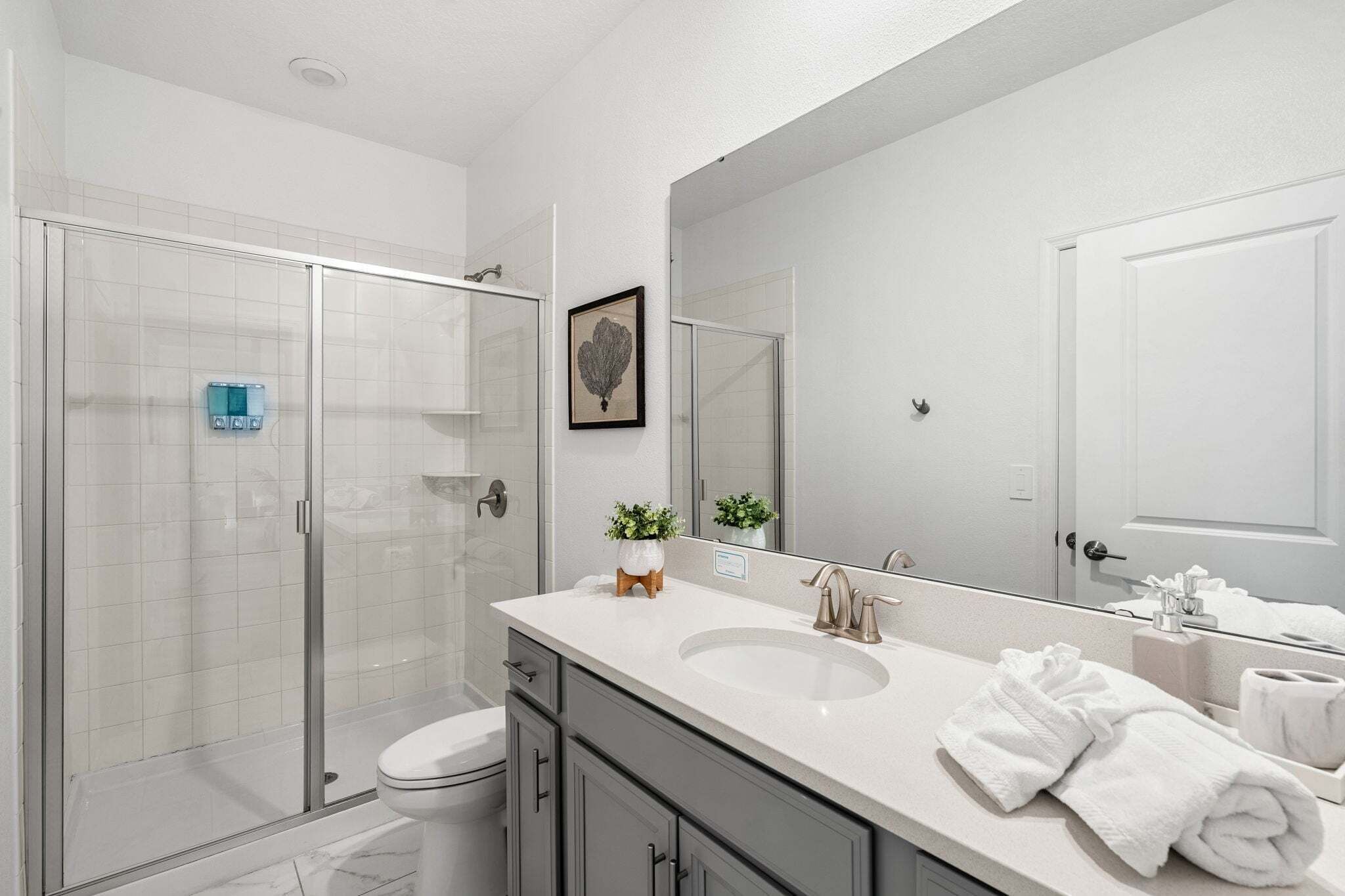 A modern bathroom with a glass shower enclosure, a large mirror, a white sink, and a toilet.