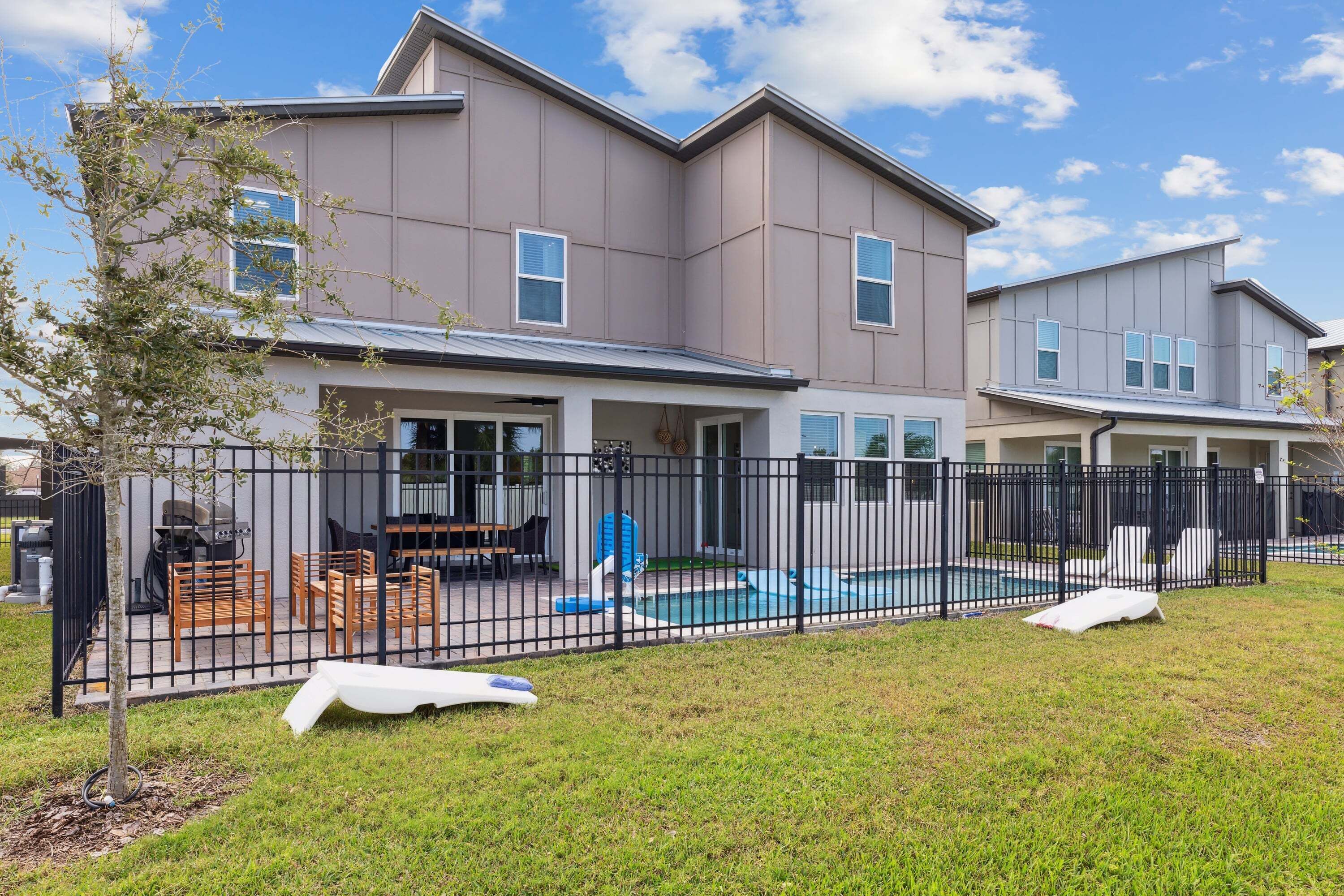 A two-story house with a fenced backyard, a pool, and outdoor furniture.