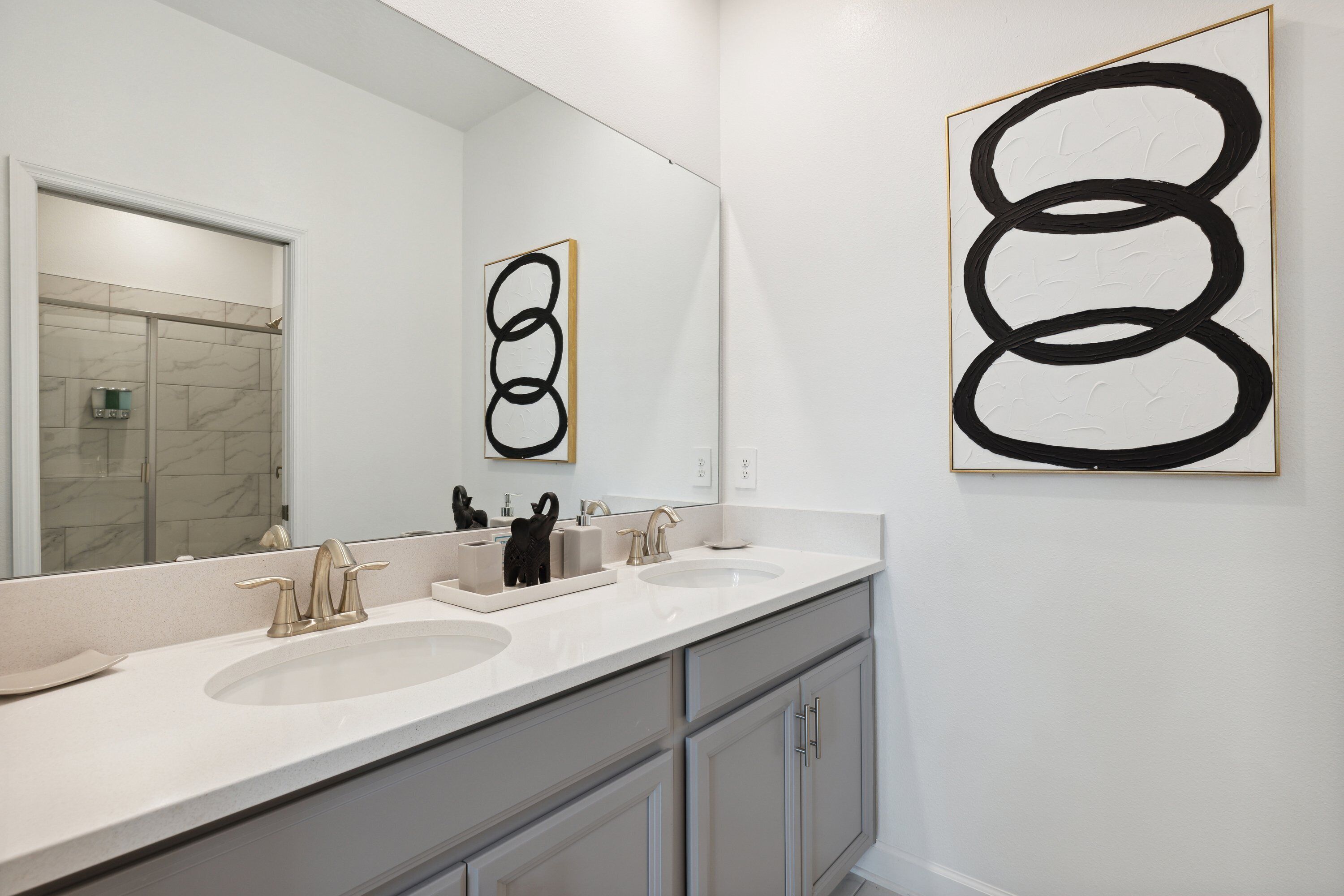 Un baño moderno con dos lavamanos, un espejo grande y un cuadro abstracto negro.