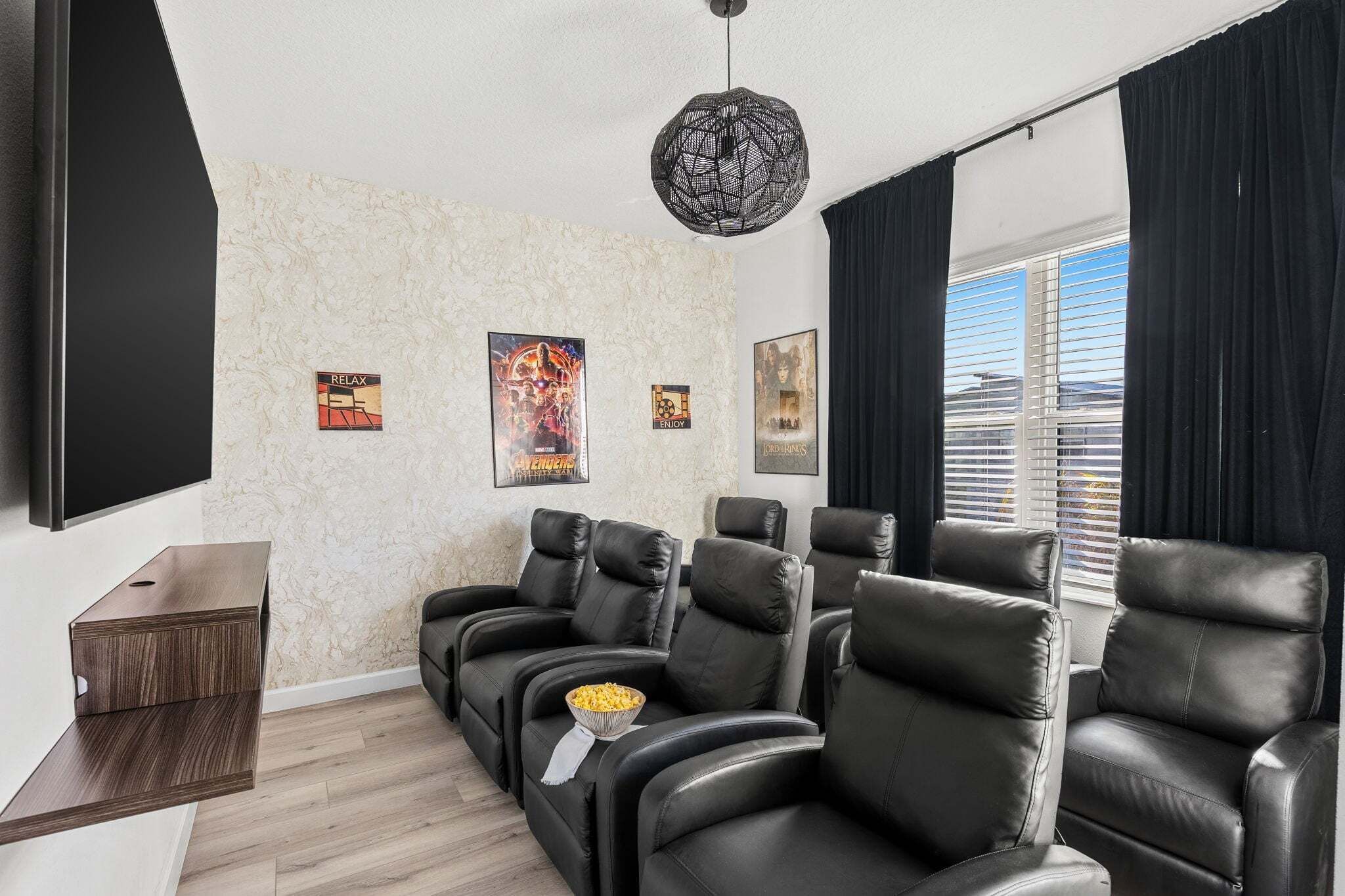 A home theater room with black leather reclining chairs, a wall-mounted TV, and a ceiling light fixture.