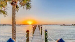 Un muelle de madera que lleva a una playa con un atardecer de fondo.