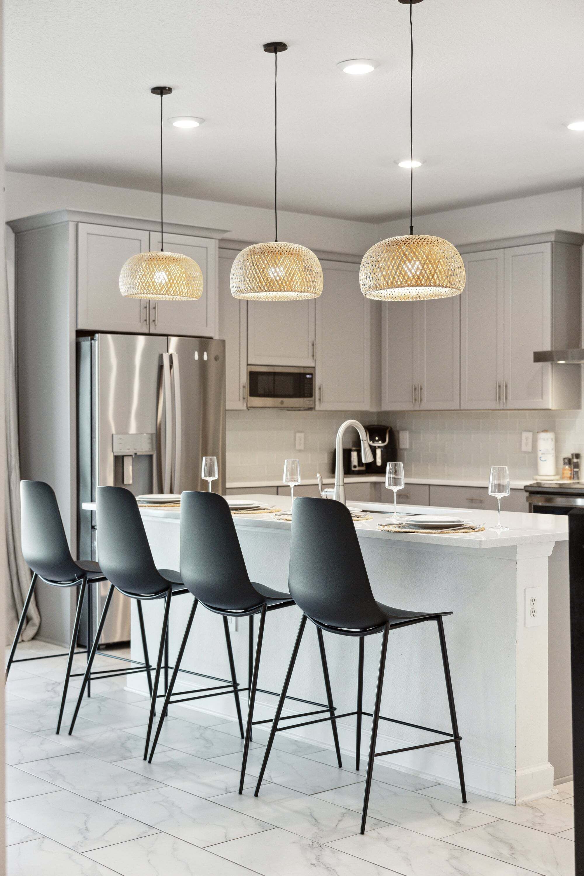 A modern kitchen with a central island, bar stools, pendant lights, and stainless steel appliances.