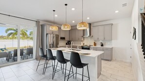 Una cocina moderna con una isla central, taburetes negros tipo bar e iluminación colgante.