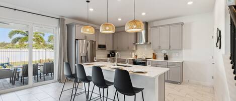A modern kitchen with a central island, black bar stools, and pendant lighting.