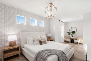 A modern bedroom with a large bed, bedside tables, a round mirror, two chairs, and a small side table. - Beachside Deluxe (Melbourne Beach)