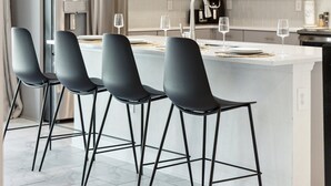 Una cocina moderna con una isla central, taburetes de bar, electrodomésticos de acero inoxidable e iluminación colgante.