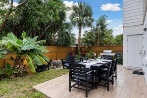 An outdoor patio with a grill, dining table, chairs, and lush tropical plants. - 10 Colonial Drive (Cocoa Beach)