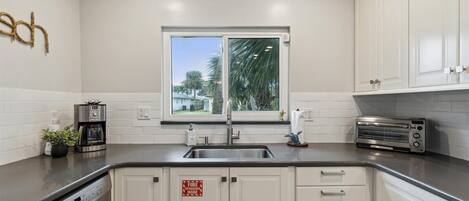 A modern kitchen with white cabinets, a stainless steel sink, a coffee maker, a toaster, and a window with a view of greenery.