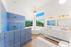 Un baño moderno con una bañera independiente, un amplio ventanal con vistas y un tocador con espejo e iluminación.