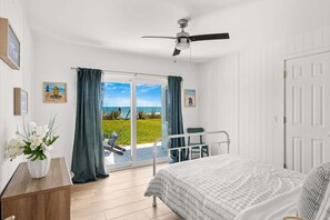 A bedroom with a bed, a ceiling fan, a view of the sea through a sliding door, and a small table with a vase of flowers. - 5435 Highway A1A (Melbourne Beach)