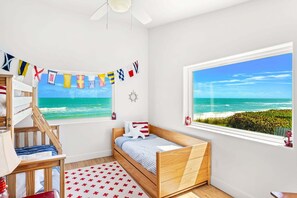 A bedroom with a wooden bunk bed, a single bed, a window with a view of the ocean, and a ceiling fan. - 5435 Highway A1A (Melbourne Beach)