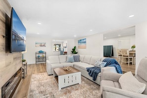 A modern living room with a sectional sofa, a coffee table, and a flat-screen TV mounted on a wooden wall. - 121 Atlantic Blvd (Indian Harbour Beach)