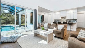 A modern living room with a sofa, coffee table, and a view of a swimming pool through large glass doors.