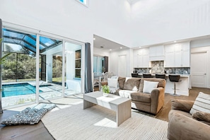 A modern living room with a sofa, coffee table, and a view of a swimming pool through large glass doors. - 139 Ocean Estates Dr (Fort Pierce)